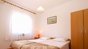 A bedroom with a bed, a nightstand, a lamp, a wardrobe, and a window with sheer curtains. - Apartment 1539 (Fazana)