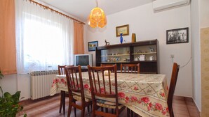 A dining area with a table set for four, surrounded by wooden chairs. A television is mounted on the wall, and there are shelves with decorative items. - Apartment 1539 (Fazana)