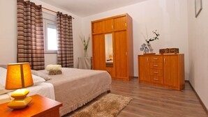 A bedroom with a bed, a wooden wardrobe, a nightstand, a lamp, and a window with curtains. - Apartment 1540 (Pula)