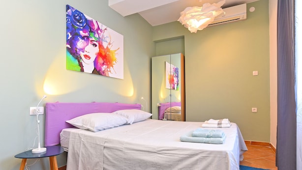 Un dormitorio con cama, mesita de noche, lámpara, espejo y un cuadro en la pared.