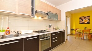 Een moderne keuken met donkerbruine kastjes, een roestvrijstalen spoelbak en een gasfornuis. Er is een eethoek met gele wanden en een tafel.