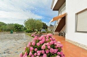 A house with a tiled patio, a covered outdoor seating area, and a garden with pink flowers. - Apartment 1552 (Pula)