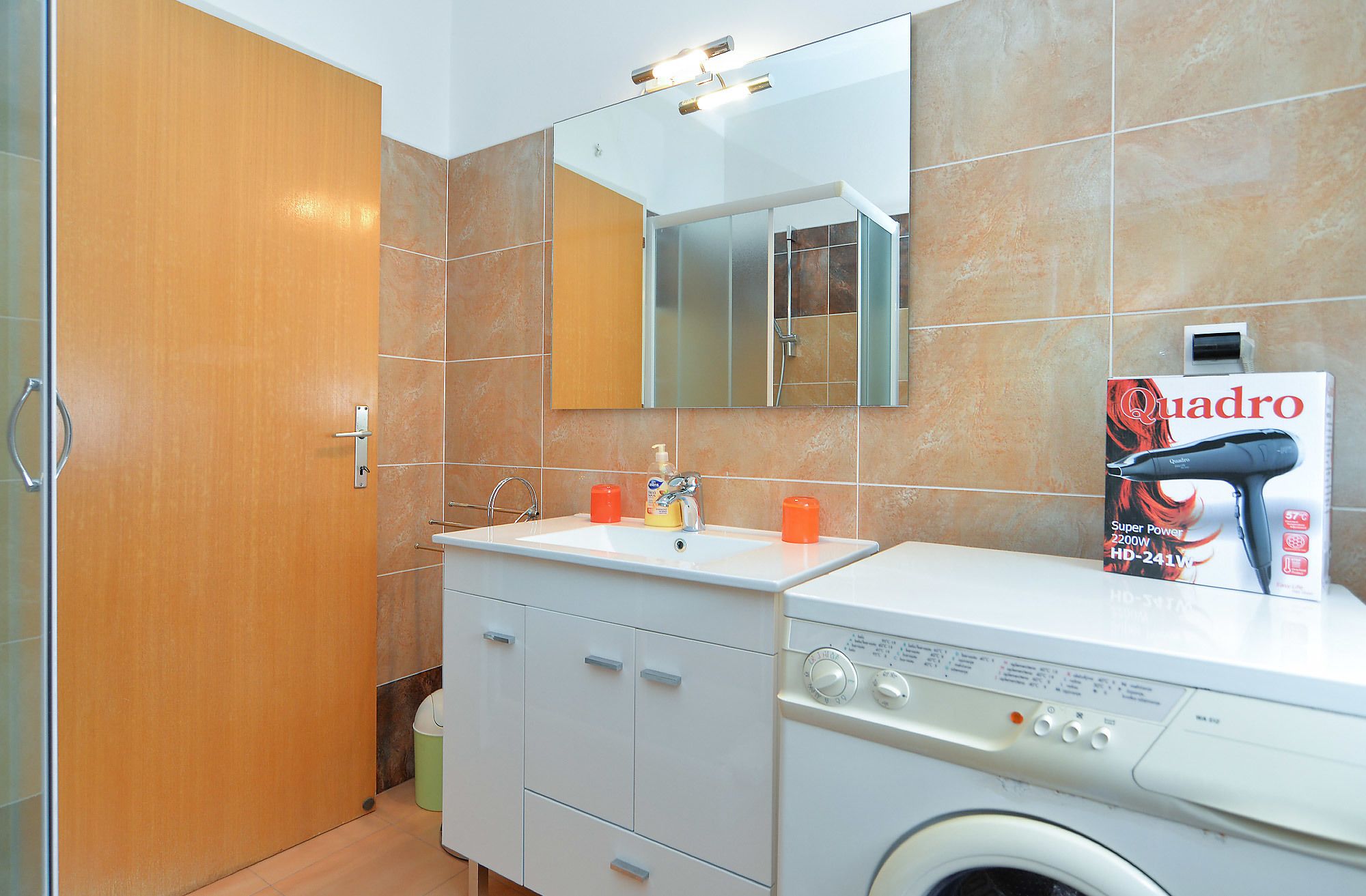 A modern bathroom with a built-in washing machine, a sink, and a mirror.
