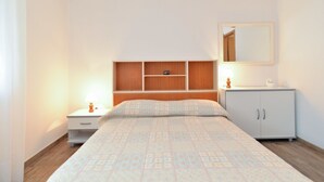 Quarto com cama, mesa de cabeceira, cômoda, espelho e prateleiras embutidas.