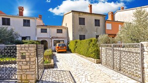Un chemin pavé de pierres menant à un bâtiment à la façade traditionnelle, avec une voiture garée et un arbuste taillé avec soin.
