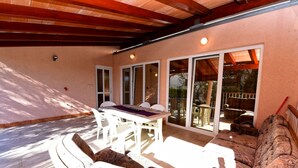 En udendørs patio med spisebord og stole, en sofa og en skydedør til en have.