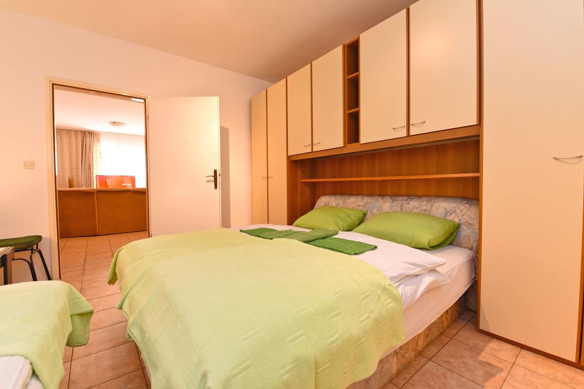 A bedroom with a bed, green pillows, a wooden wardrobe, and a small table.