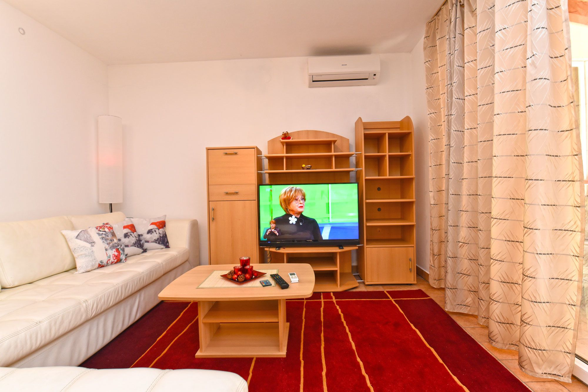 A living room with a sofa, a coffee table, a TV, wooden shelves, and a red carpet.