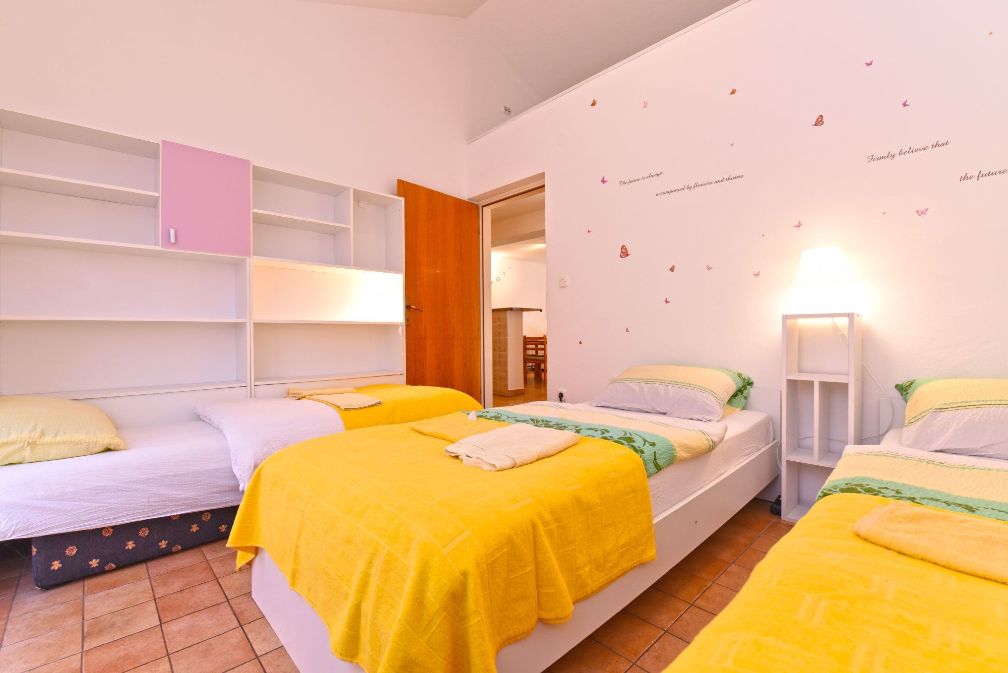 Un dormitorio con tres camas, cada una con una manta amarilla, almohadas blancas y una puerta de madera.