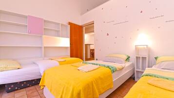 Un dormitorio con tres camas, cada una con una manta amarilla, almohadas blancas y una puerta de madera.