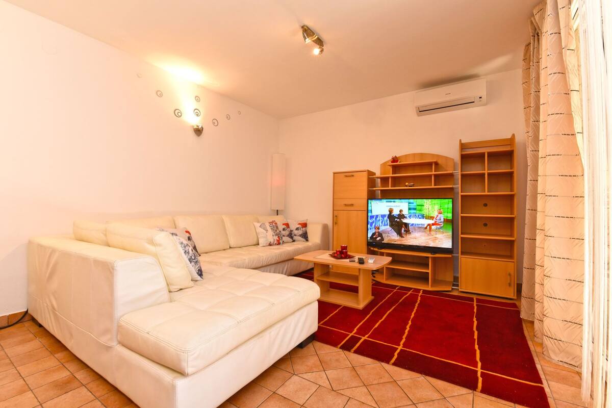 A living room with a beige sofa, a television, wooden shelves, and a red carpet.