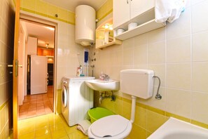 A compact bathroom with a washing machine, toilet, sink, and a bathtub. - Apartment 1562 (Pula)