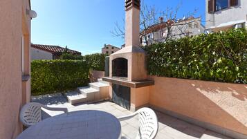 An outdoor patio with a stone oven, a round table, and two white chairs.