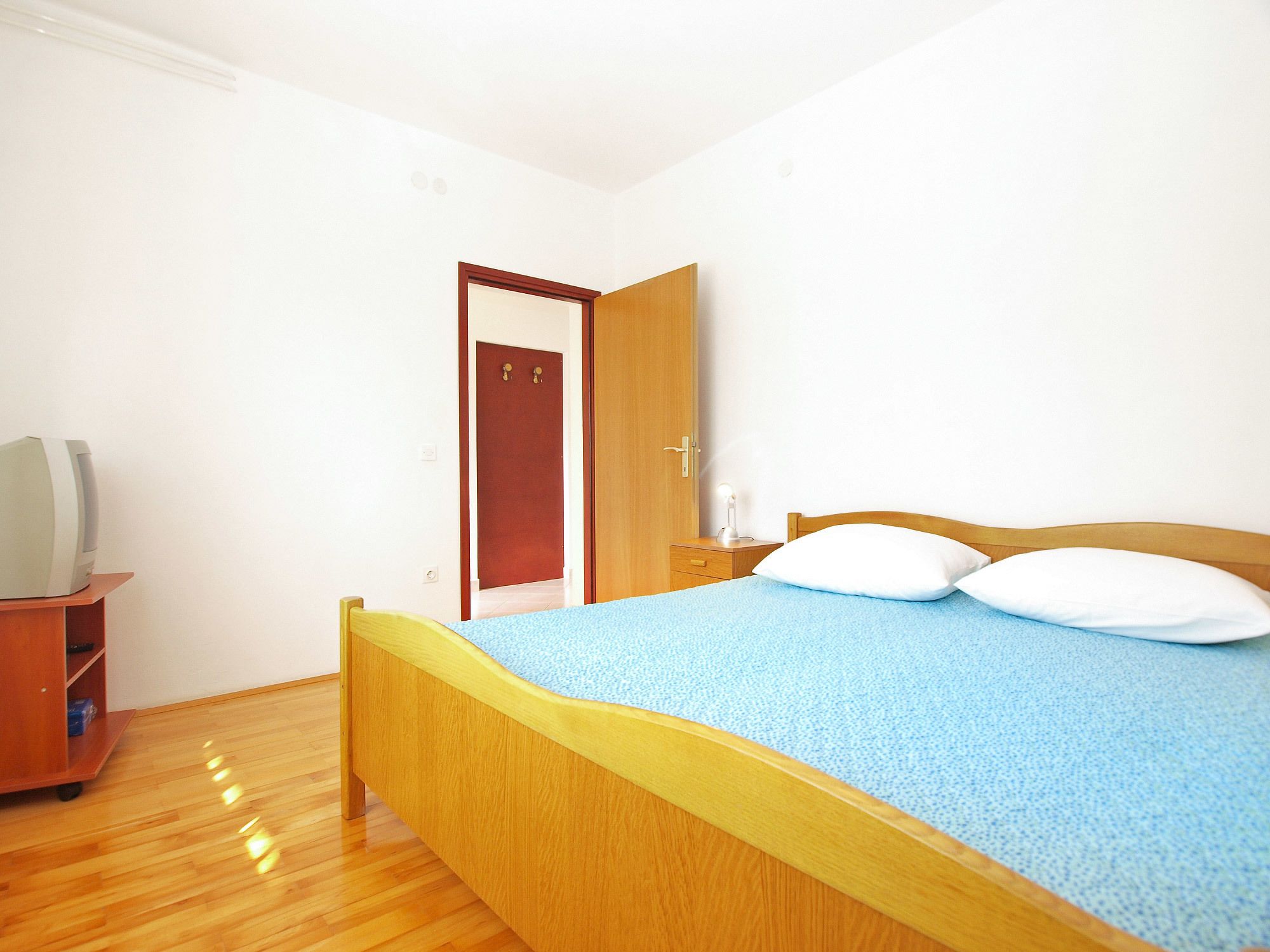 A bedroom with a wooden bed, a nightstand, a desk with a lamp, and a wardrobe.