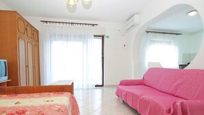 A hotel room with a bed, a pink sofa, a wooden wardrobe, and a bathroom visible through a glass door. - Apartment 1563 (Pula)