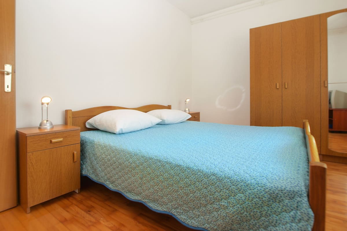 A bedroom with a wooden bed, a nightstand, a drawer, a wardrobe, and a mirror.