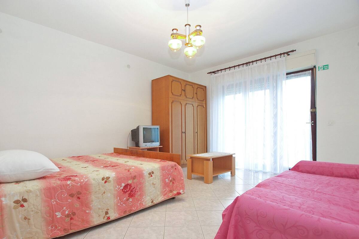 A hotel room with two beds, a wooden wardrobe, a television on a small table, and a chandelier.