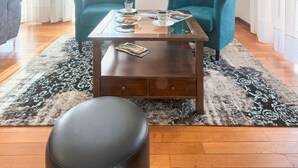Una sala de estar con dos sillones color turquesa, una mesa de centro y un otoman negro. Un cuadro de una escena portuaria cuelga en la pared.