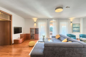 A modern living room with a grey sofa, wooden flooring, a television, and a glass cabinet.