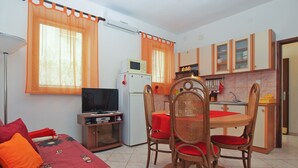 A compact living space with a kitchenette, a dining area with a table and chairs, a television on a stand, and a bed with a patterned cover. - Apartment 1569 (Pula)