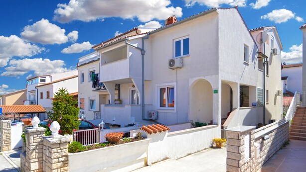 A two-story residential building with a balcony, a satellite dish, and a small garden area with flowers. - Apartment 1569 (Pula)