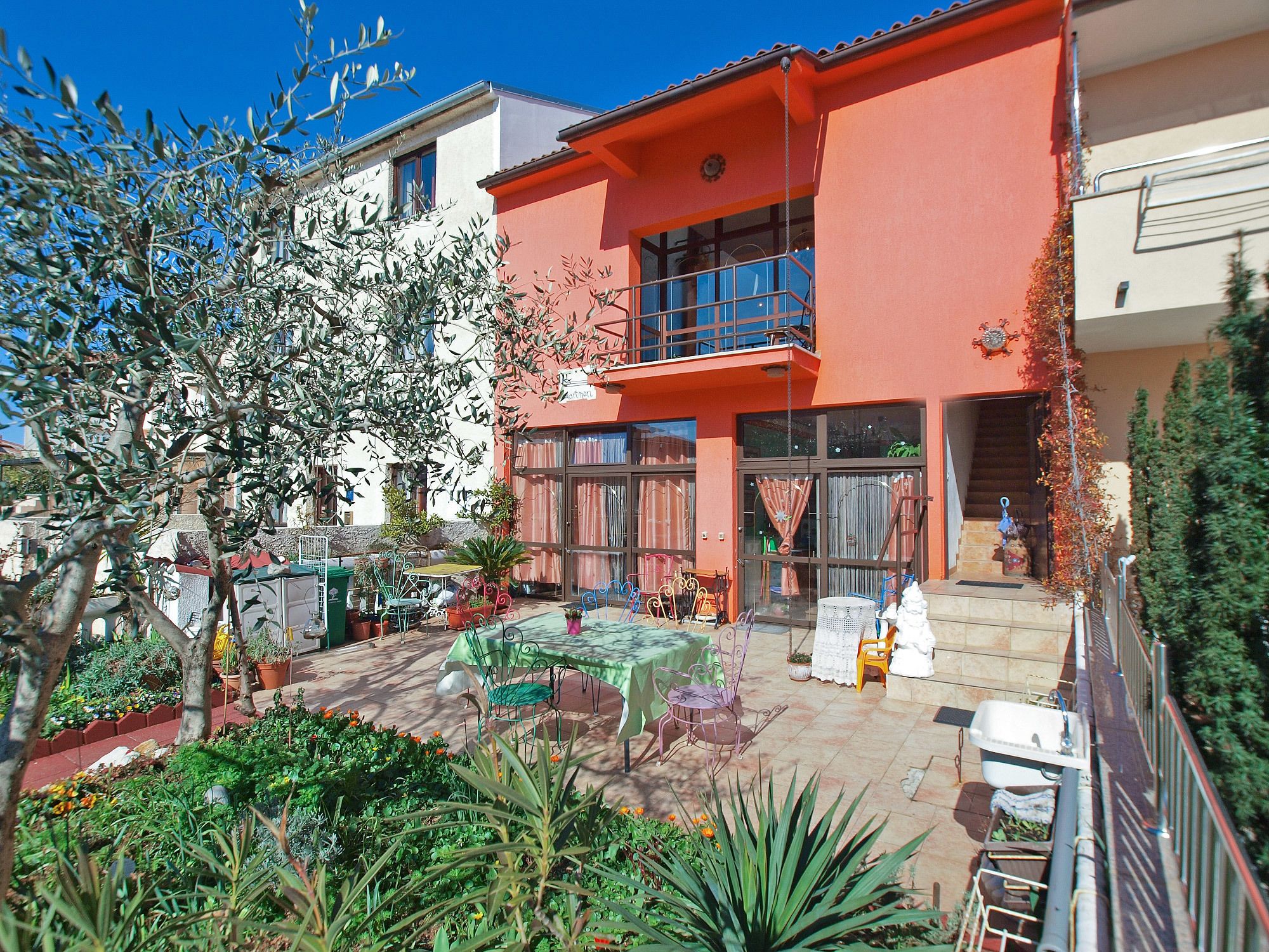 A courtyard with a table and chairs, potted plants, and a staircase leading to a balcony.