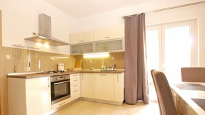 A modern kitchen with a gas stove, oven, and a dining area with a table and chairs. - Apartment 1573 (Fazana)