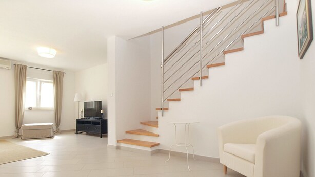 A modern living room with a staircase, a flat-screen TV, a sofa, and a small table. - House 1581 (Pula)