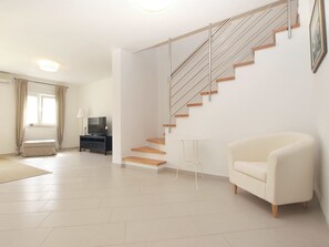 A modern living room with a staircase, a flat-screen TV, a sofa, and a small table. - House 1581 (Pula)