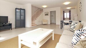 A modern living room with a white sofa, a coffee table, a TV on a stand, a cabinet, and a staircase leading to another room. - House 1581 (Pula)