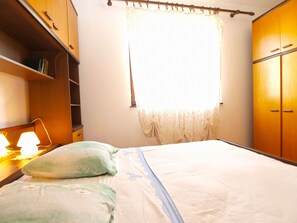 A bedroom with a bed, a nightstand with a lamp, a wardrobe, and a window with curtains.