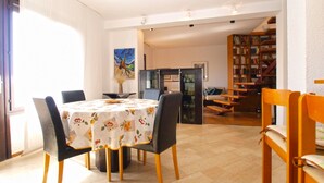 A dining area with a table set for four, surrounded by chairs. There is a kitchen area with a refrigerator and a dining table. A staircase leads to a loft area with a bookshelf. - Apartment 1583 (Medulin)