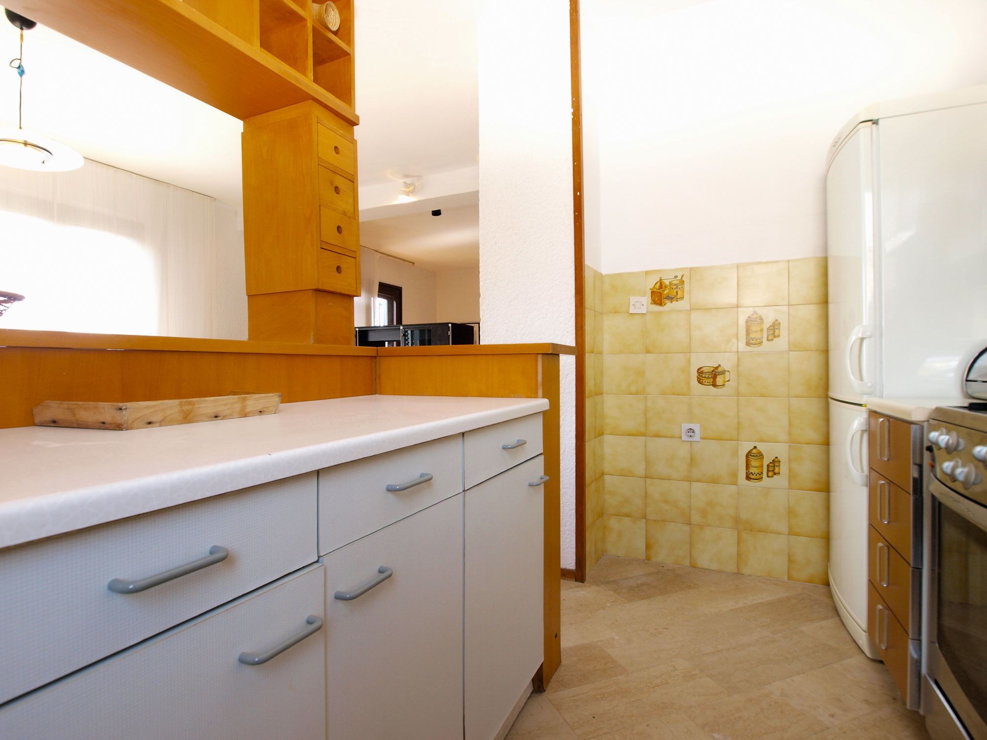 A kitchen with white cabinets, a white countertop, a stainless steel refrigerator, and yellow-tiled backsplash.