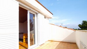 A balcony with a tiled floor, a sliding glass door leading to a room with a bed and a wooden chair, and a clear view of the sky and distant buildings. - Apartment 1583 (Medulin)