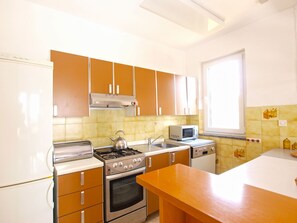 Kitchen features a stove, kettle, microwave, and dishwasher, with a tiled backsplash and natural light from a window.