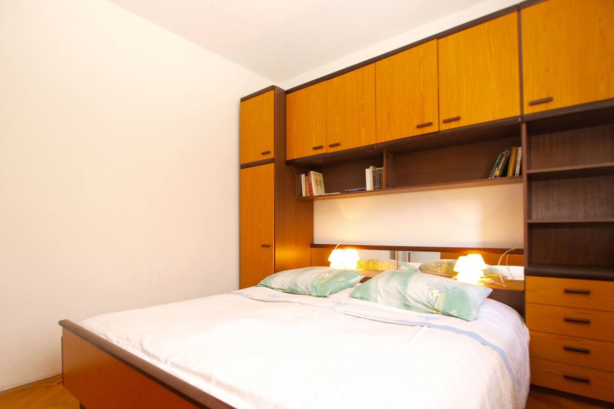 A bedroom with a wooden bed frame, a large wardrobe, and a bedside table with a lamp.
