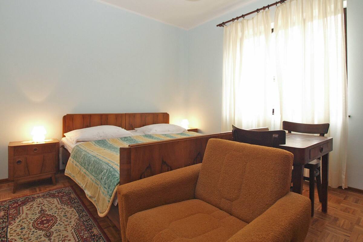 A bedroom with a wooden bed, a nightstand, a chair, a desk, and a window with curtains.