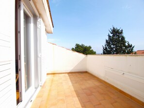 A balcony with a tiled floor, white walls, and a door leading to an interior space.
