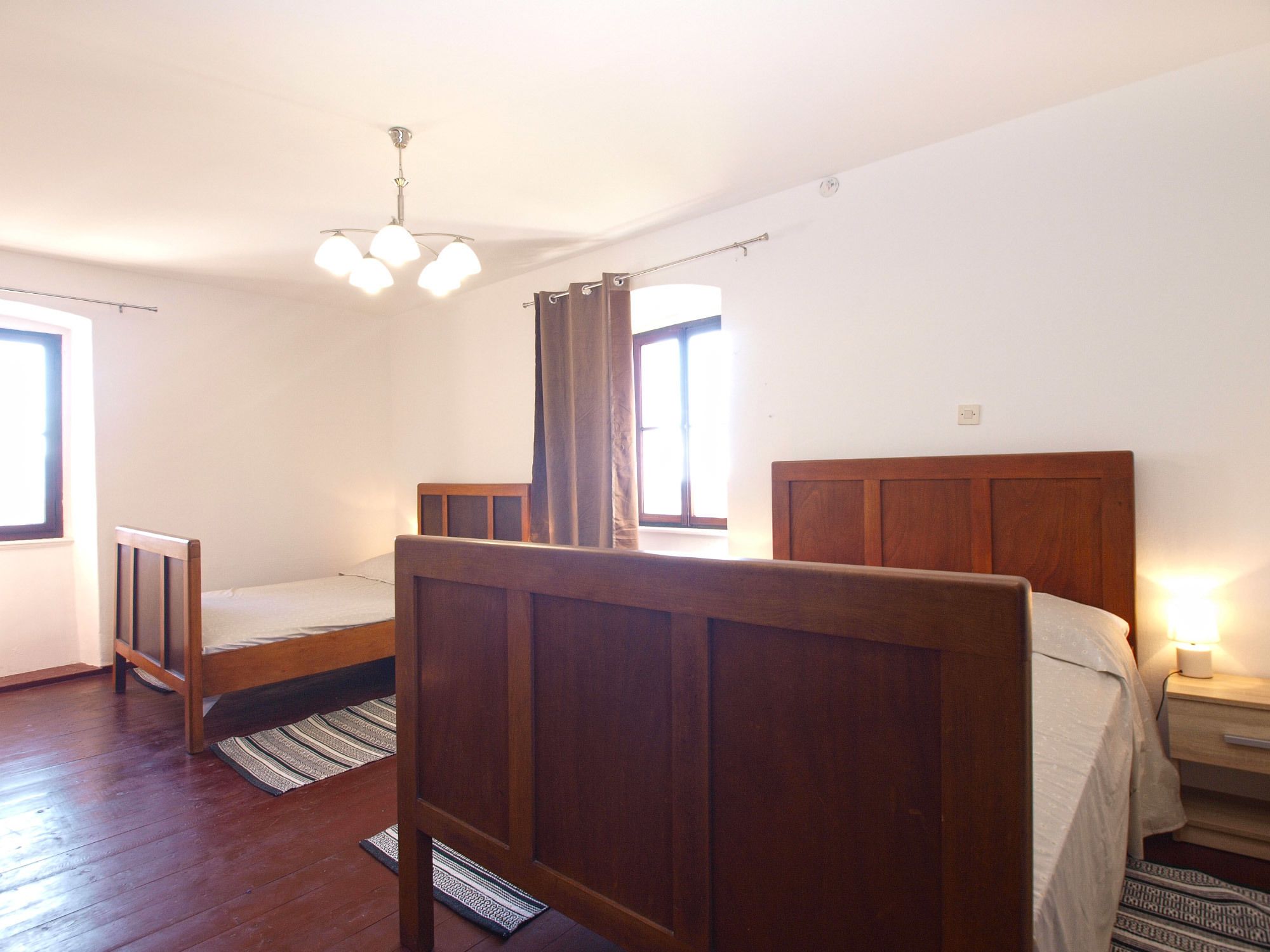 Ein Schlafzimmer mit einem hölzernen Bett, einem Nachttisch, einem Fenster und einer Deckenleuchte.