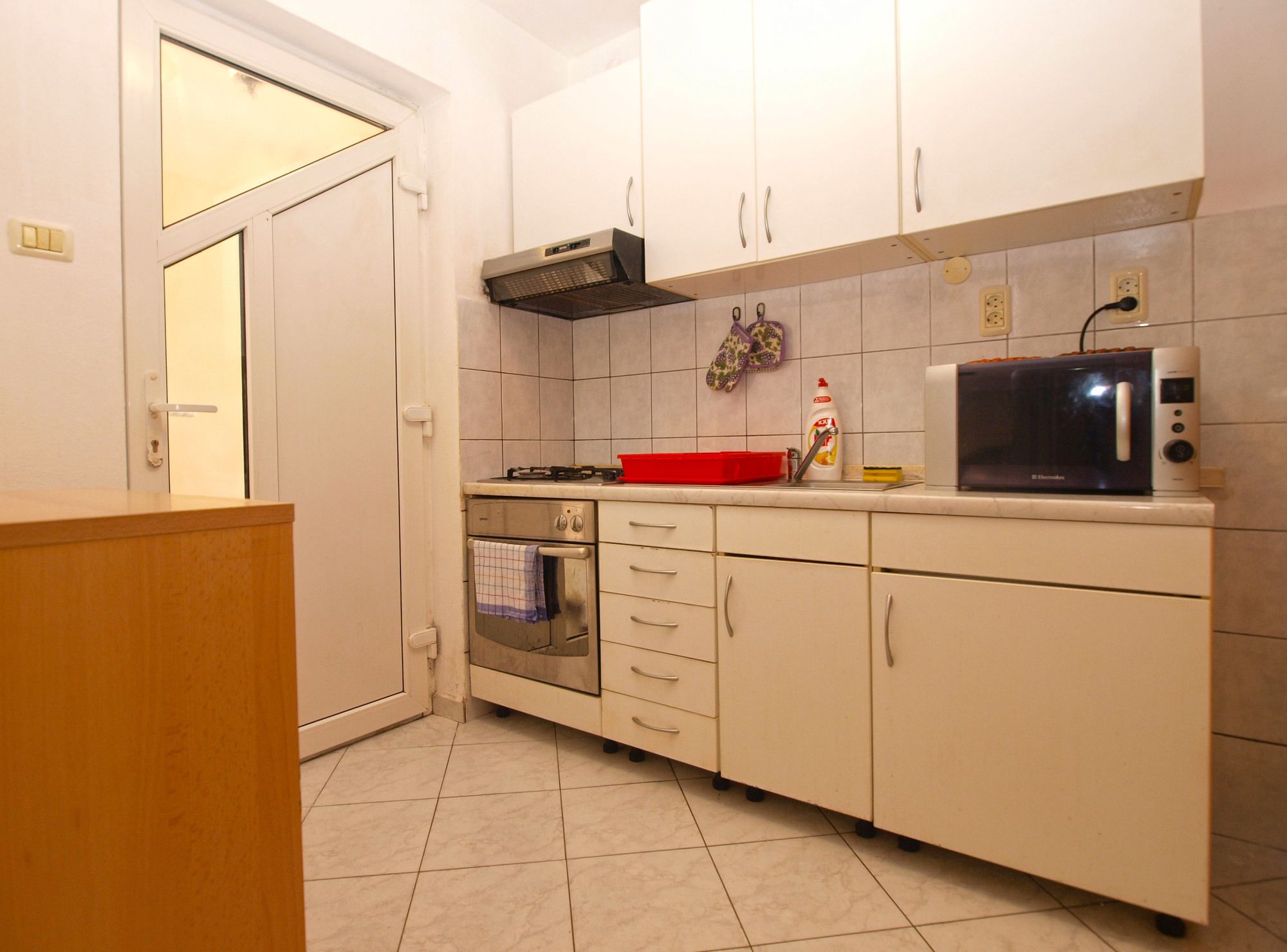 A compact kitchen with white cabinets, a built-in oven, a microwave, and a red cutting board.
