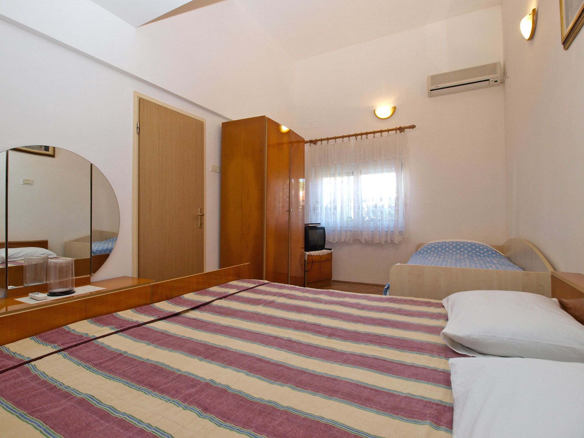 A bedroom with a bed, a mirror, a wardrobe, a television, and a window with curtains.