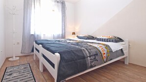 Une chambre à coucher avec un lit, une table de chevet, une lampe de table et une lampe sur pied, ainsi qu’une fenêtre avec des rideaux.