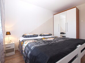 A bedroom with a bed, a nightstand, a lamp, a wardrobe, and a mirror. - Apartment 1592 (Pula)
