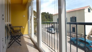 Un balcon avec un mur jaune, une chaise et une vue sur une rue bordée de voitures et d’immeubles.