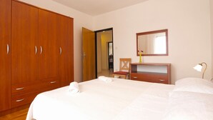 Een hotelkamer met een grote houten garderobe, een bed met witte lakens, een nachtkastje met een lamp en een spiegel aan de muur.