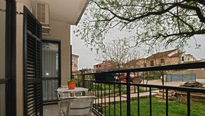 Een balkon met een tafel en stoelen, een bloempot en uitzicht op een straat met gebouwen en een geparkeerde tractor.