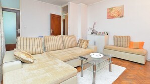 Uma sala de estar com um sofá bege, uma mesa de centro de vidro e um tapete branco.