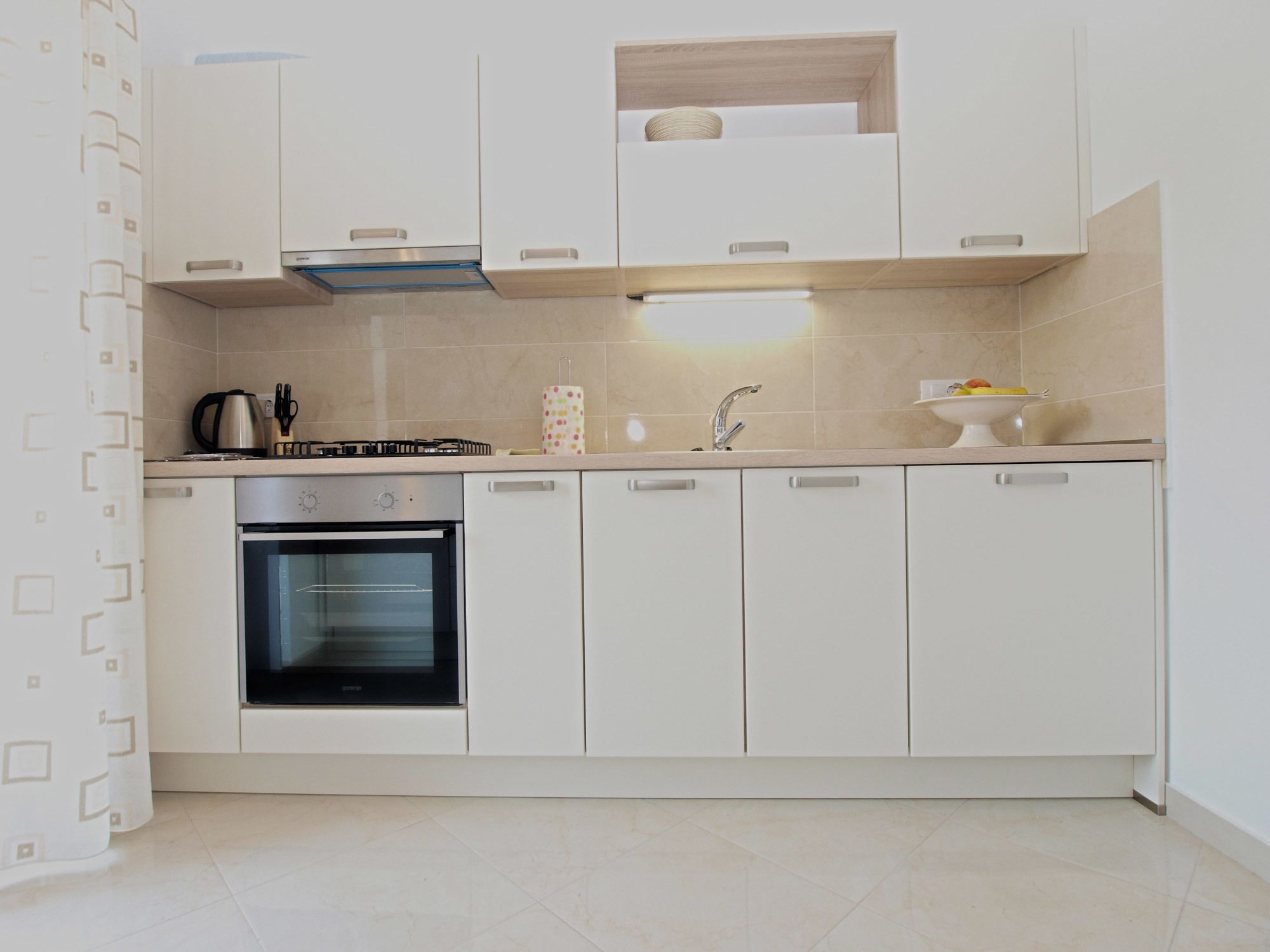 A modern kitchen with white cabinetry, a built-in oven, and a countertop with a kettle and utensils.