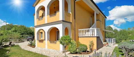 A two-story building with a yellow facade, arched windows, and a balcony with white balustrades.