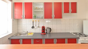 A kitchen with red cabinets, a stainless steel sink, a gas stove, and a kettle.